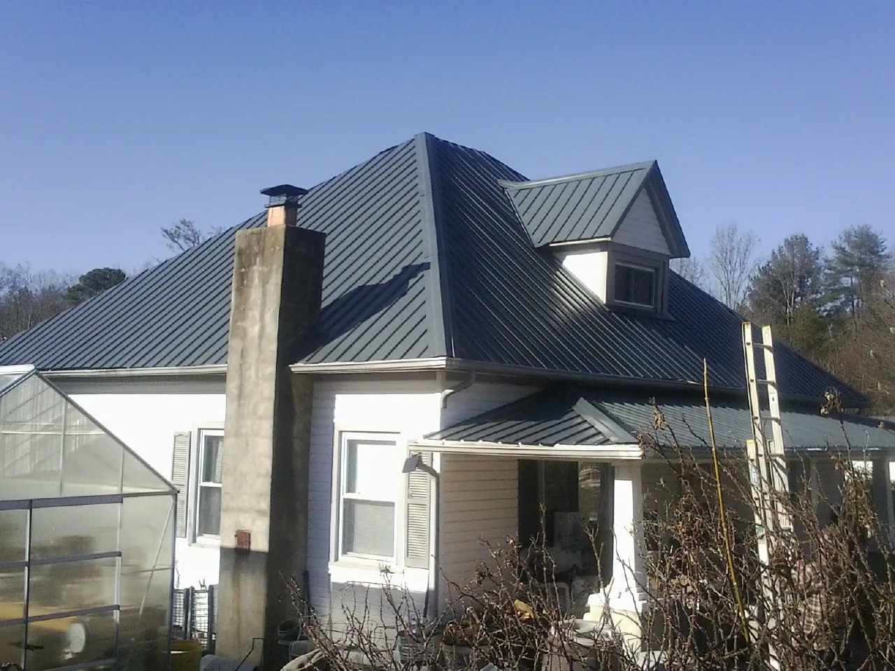 Dark blue standing seam metal roof on a white farmhouse with dormer — Slate & Tile Roof Repair by Roofing Brothers in De Graff