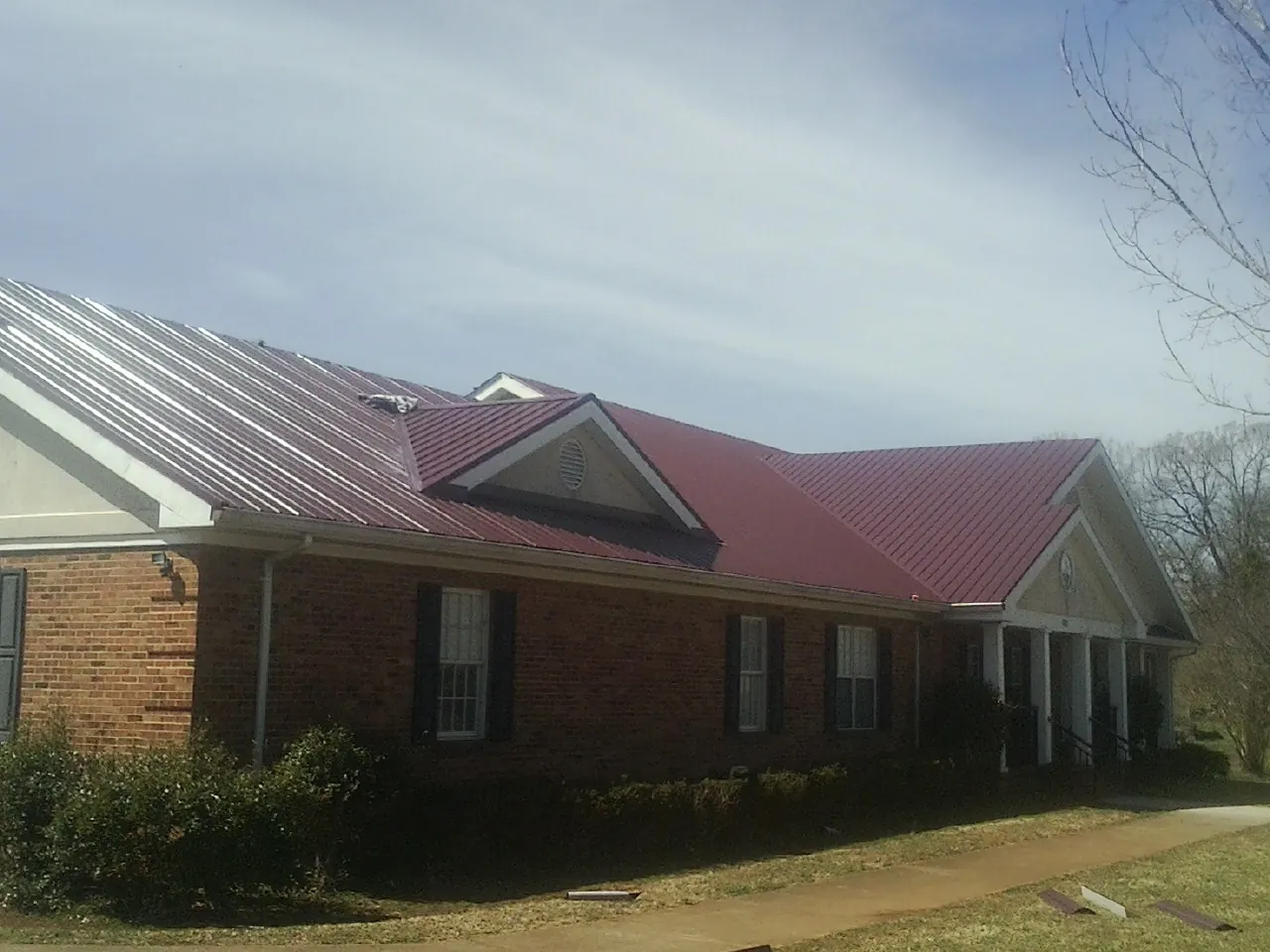 Red metal roof with gabled entries on a long brick building, from a Hail Damage Roof Repair job in De Graff