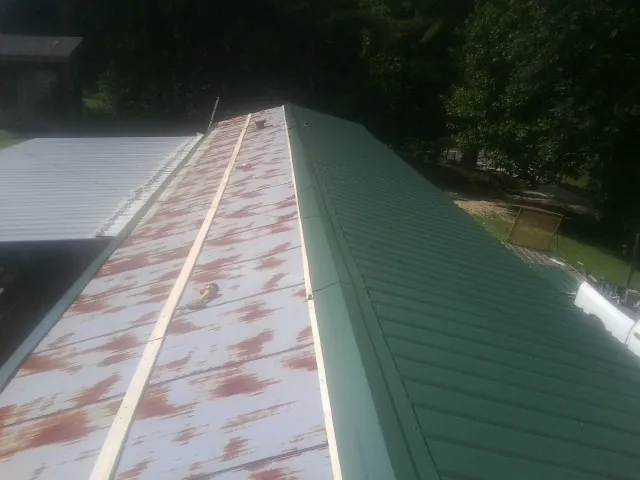 Old rusted panels beside newly installed green metal roofing — Wind Damage Roof Repair by Roofing Brothers in De Graff