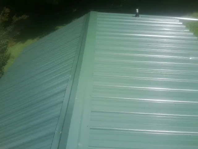 New green metal panels meeting at the ridge of a roof — Flat Roof Repair work by our crew in De Graff