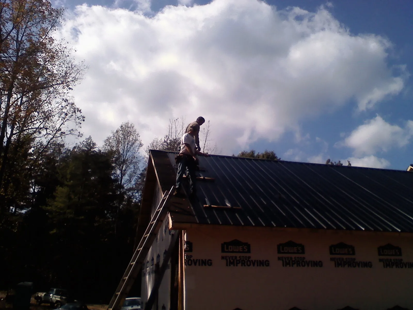Roofer fastening dark metal panels high against a cloudy sky, from a Roof Inspection job in De Graff